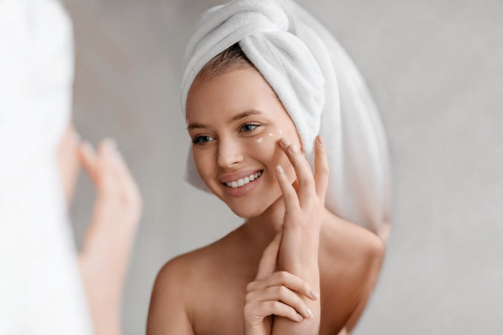 Rituel beauté quotidien avec les soins Derma'Love : sourire radieux devant le miroir après l'application de nos formules bio certifiées. Le teint lumineux et la peau veloutée témoignent de l'efficacité de notre routine naturelle.