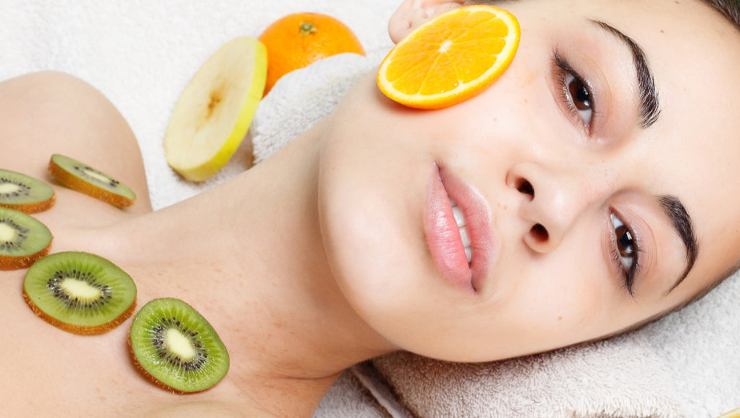 Rituel beauté Derma'Love : peau éclatante entourée de fruits frais vitaminés (orange, kiwi, pomme) illustrant les actifs naturels de nos soins visage. Mise en scène des ingrédients riches en vitamine C et antioxydants, symbolisant notre engagement pour une cosmétique naturelle et efficace.
